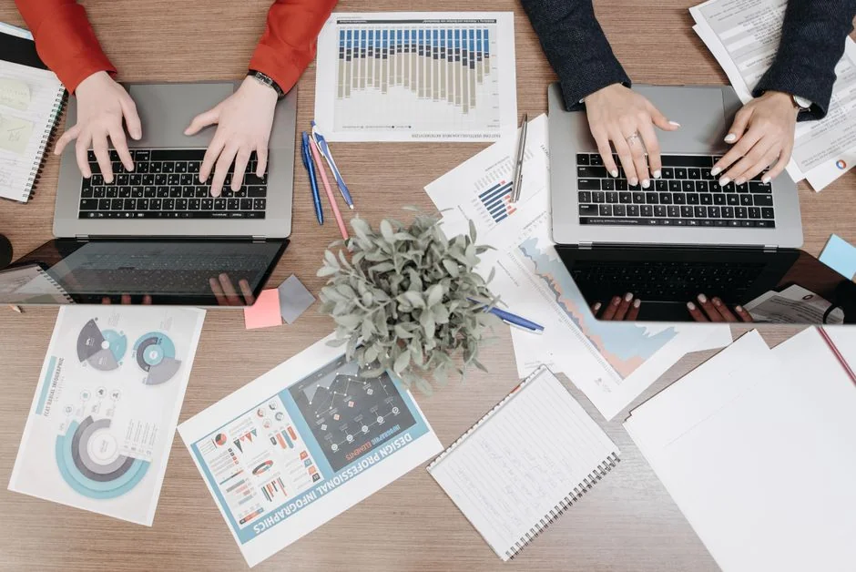 A team of colleagues discussing sales growth using a digital tablet and computer screen in an office setting.